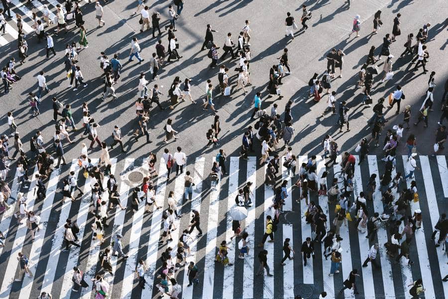 Eine große Gruppe von Menschen überquert eine Straße in Tokio, während sie von einem vorbeifahrenden Taxi beobachtet wird.