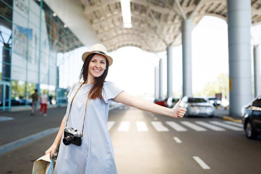 Eine Frau in Kleid und Hut steht in der Warteschlange für ein Flughafentaxi.