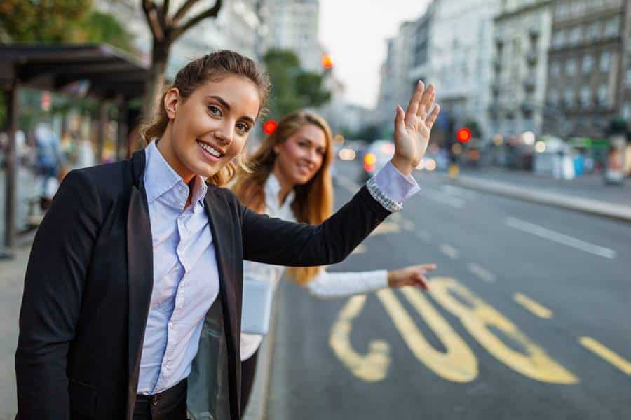 Zwei Geschäftsfrauen winken auf der Straße einem vorbeifahrenden Taxi in Geretsried zu.