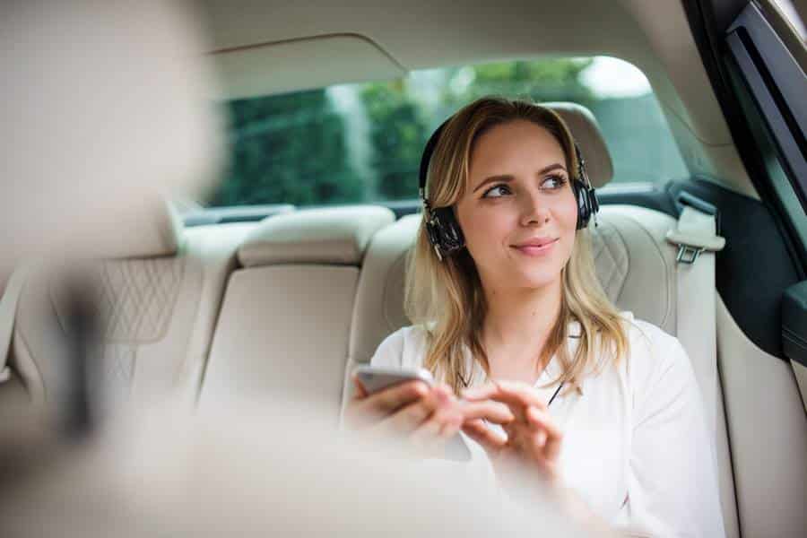Eine Frau sitzt auf dem Rücksitz eines Taxis und schaut auf ihr Telefon.