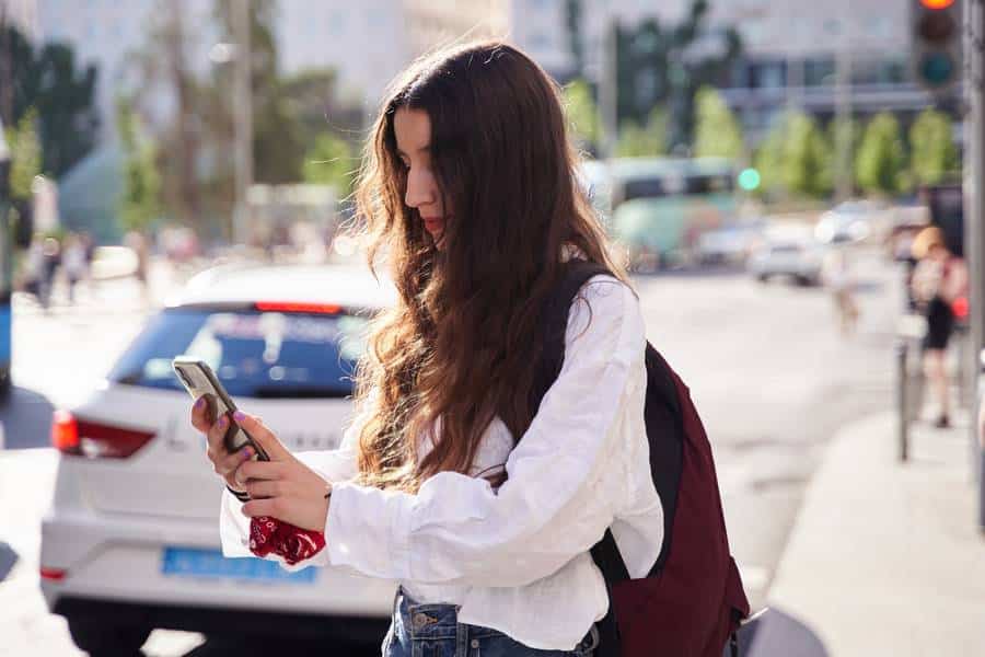 Eine junge Frau schaut auf ihr Handy, während sie auf der Straße in Homburg auf ein Taxi wartet.