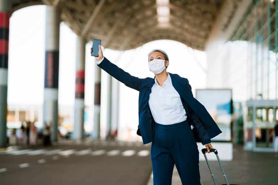 Eine Frau mit Mundschutz macht am Flughafen ein Selfie, bevor sie in ihr Taxi nach Idar-Oberstein steigt.