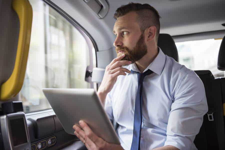 Ein Mann sitzt auf dem Rücksitz eines Taxis und benutzt ein Tablet.